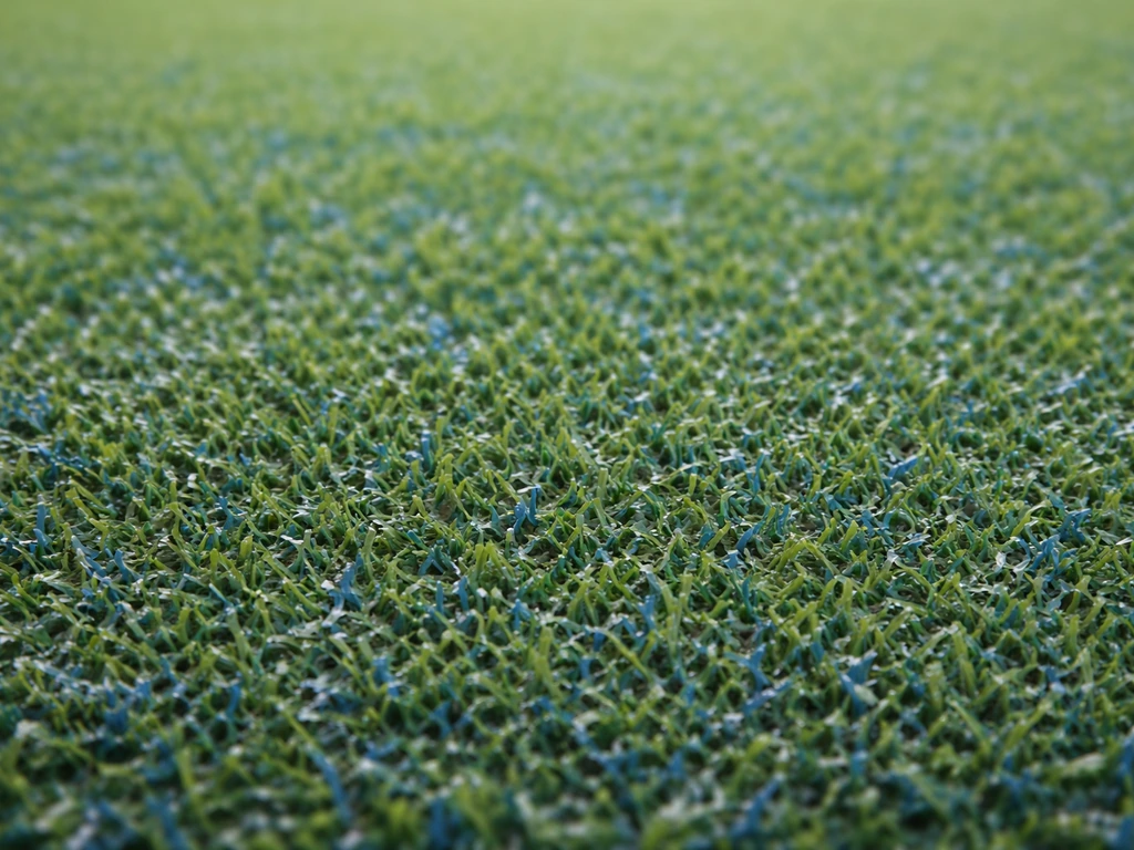 Gazon artificiel de hockey en gros plan, fibres vertes et teintes bleutées visibles, texture détaillée.